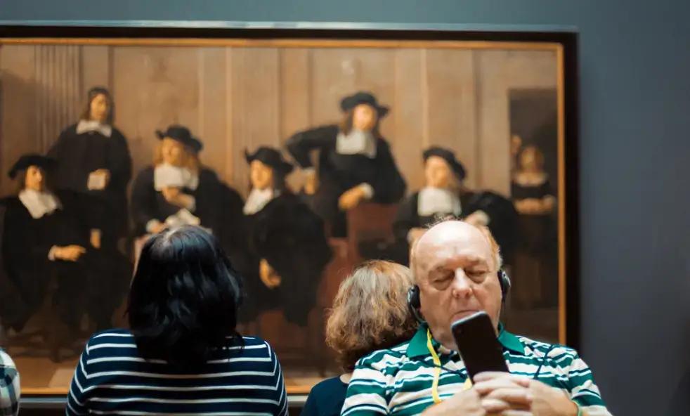 Museum visitor listening to audio guide near classic Dutch group portrait