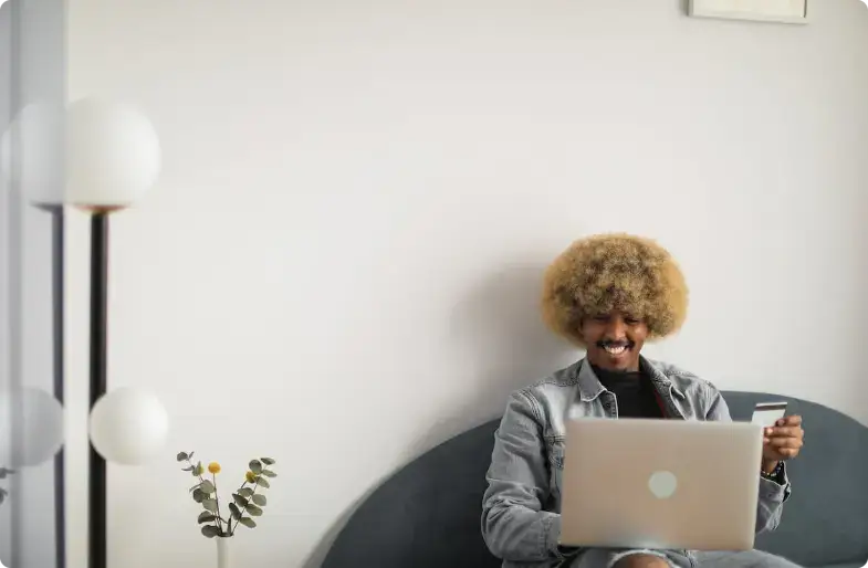 Glimlachende persoon met krullend haar die op een laptop werkt bij een lamp en plant