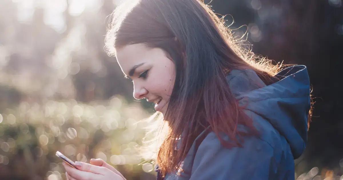 Personne en veste bleue souriante utilisant un smartphone à l'extérieur
