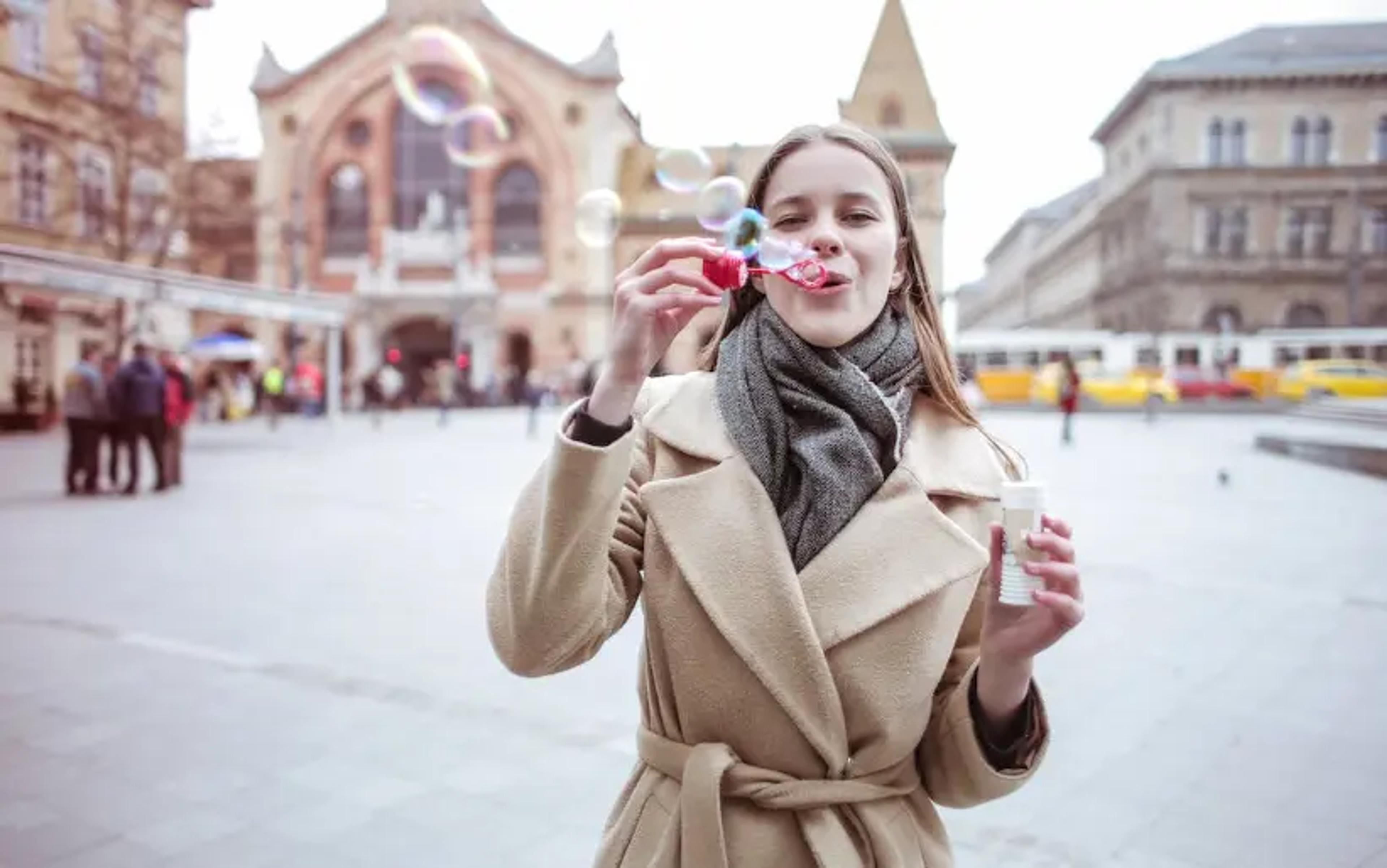 Mujer soplando burbujas con abrigo de invierno en la calle de la ciudad con edificios históricos
