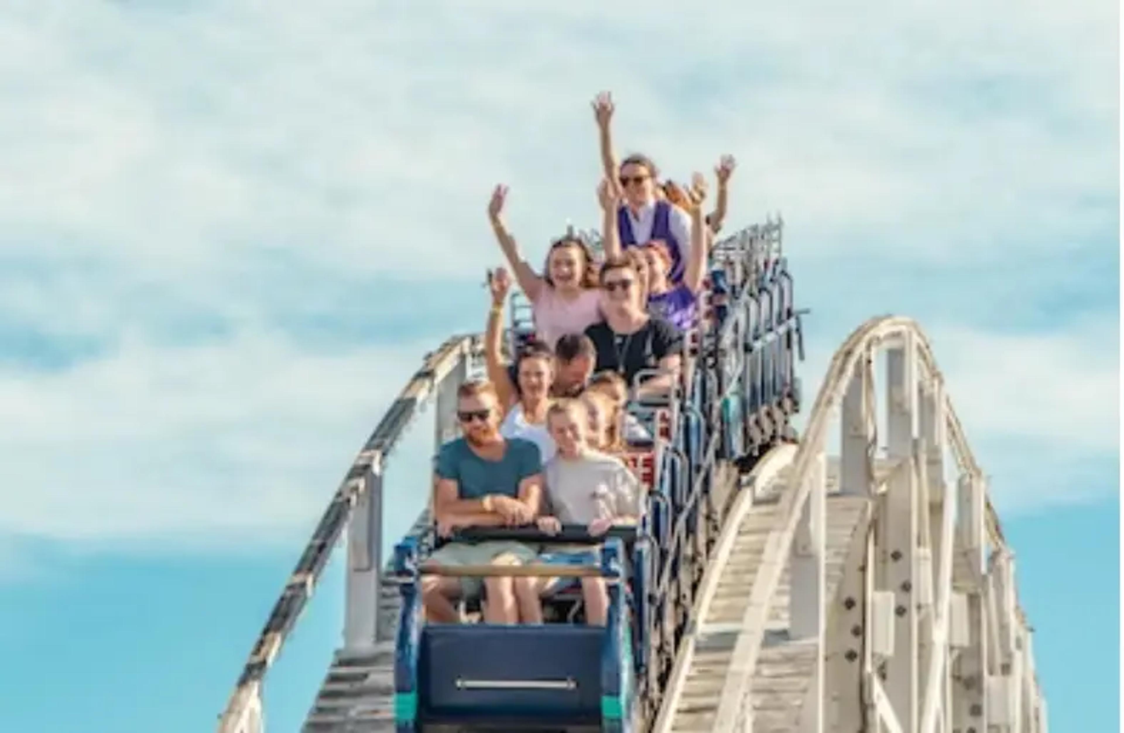 Excited riders on a white wooden roller coaster with blue sky background