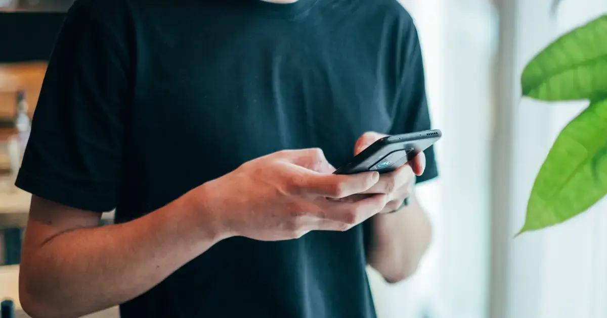 Personne en t-shirt noir utilisant un smartphone près d'une plante verte