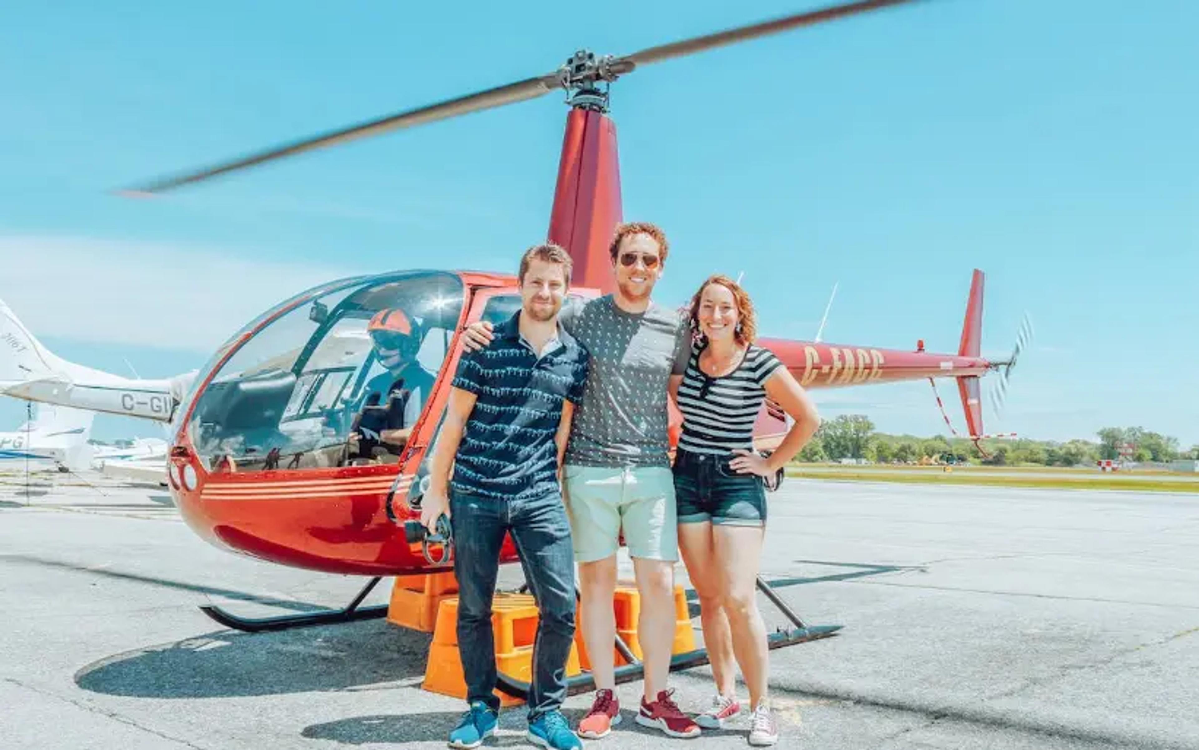 Trois amis posant devant un hélicoptère rouge par une journée ensoleillée