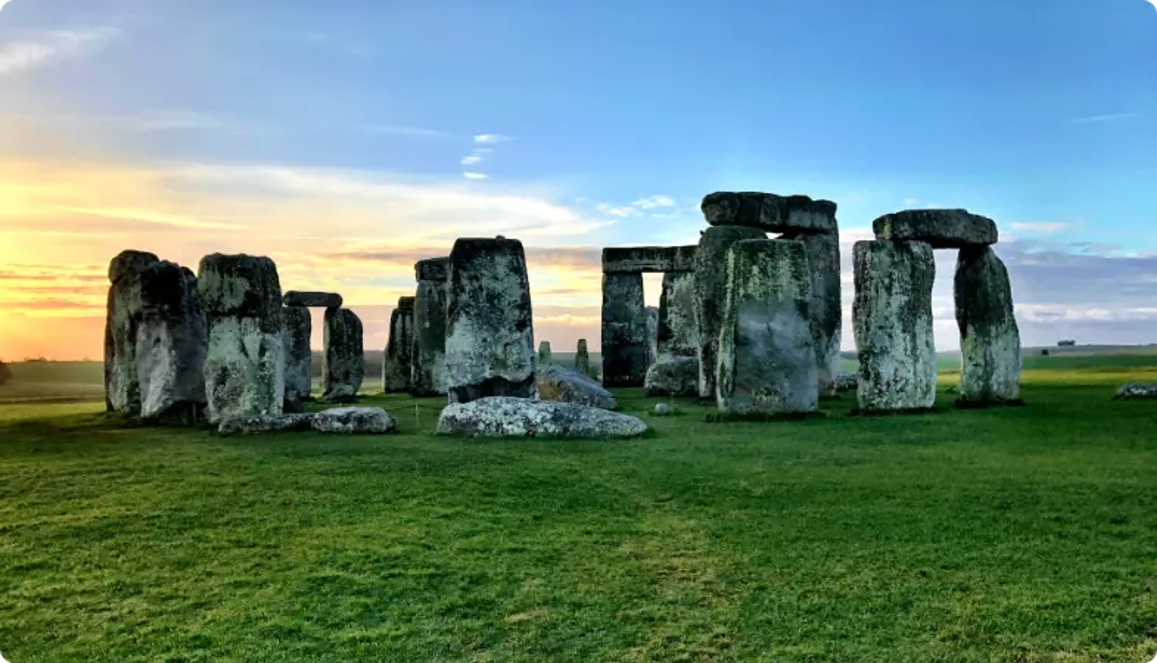 Monument préhistorique de Stonehenge au lever du soleil avec un ciel dramatique et un champ vert