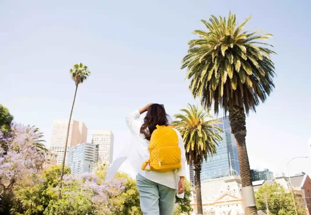 Pessoa com mochila amarela a olhar para a paisagem urbana com palmeiras