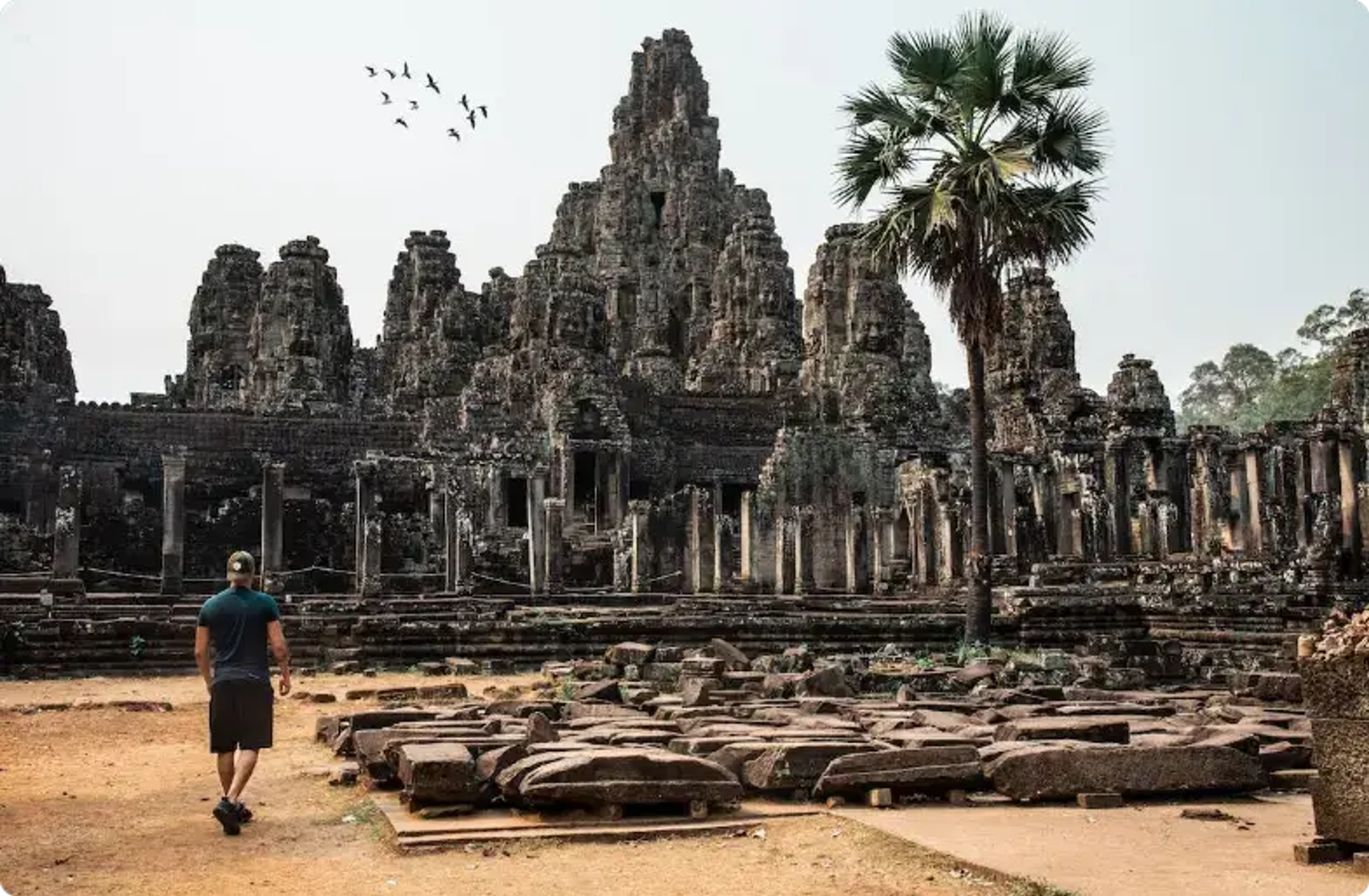 Ősi Bayon templom Angkor Thom-ban, Kambodzsában, kő tornyokkal és pálmafával