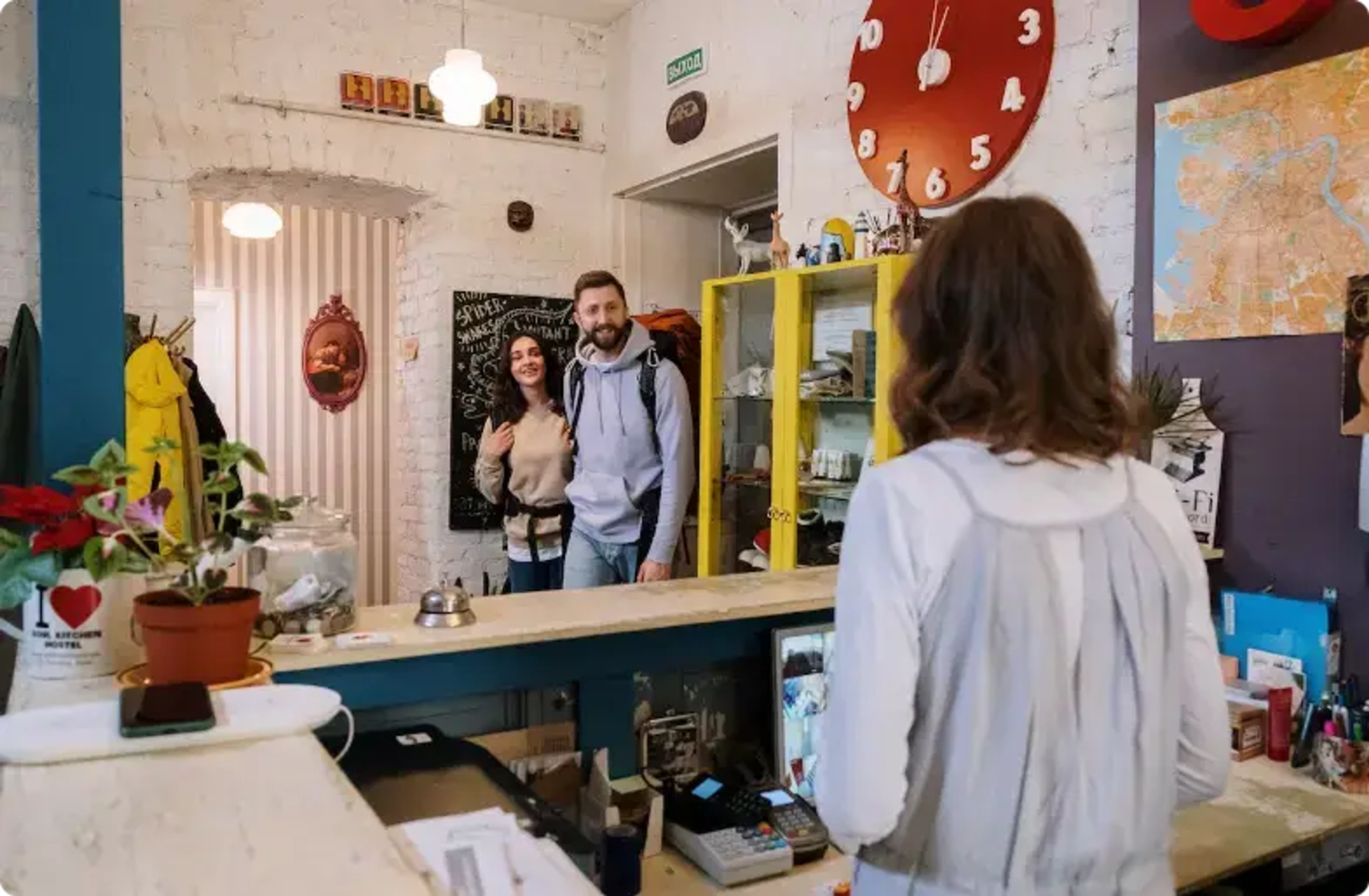 To kunder ved kaffebarens disk med barista, gule hylder og planter
