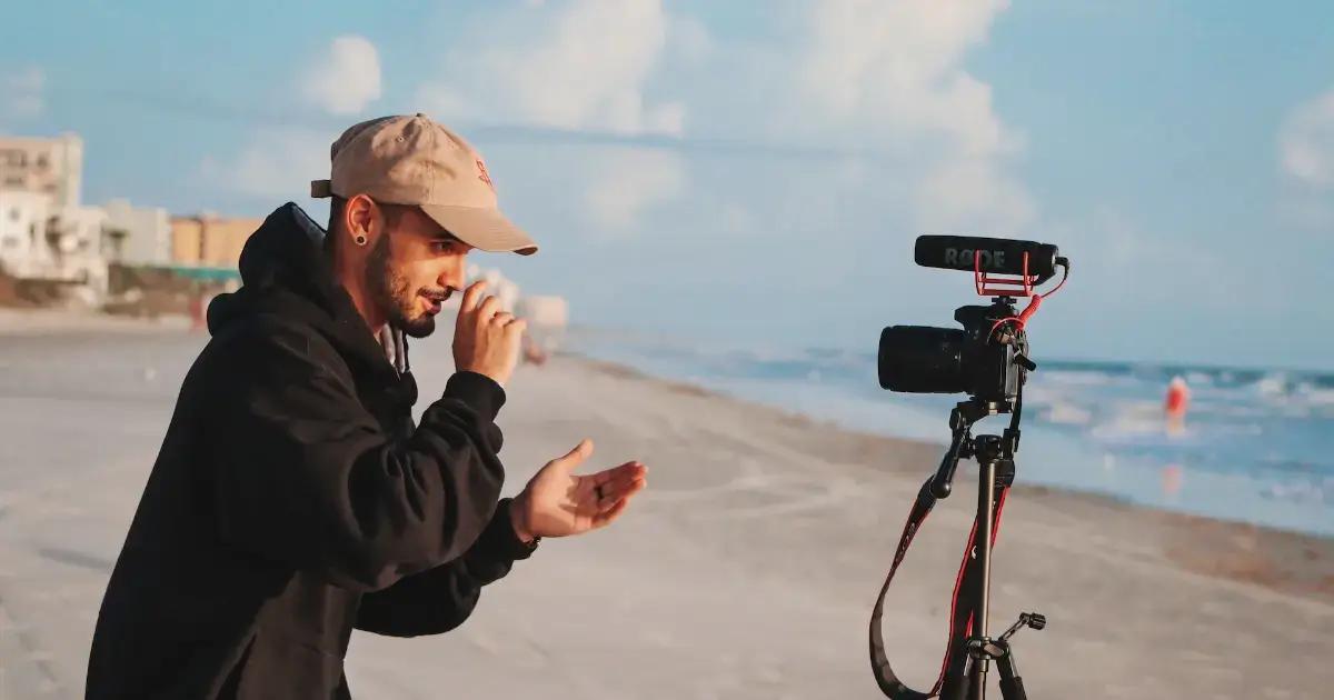 Videograf i sort hættetrøje optager på stranden med professionelt kamera