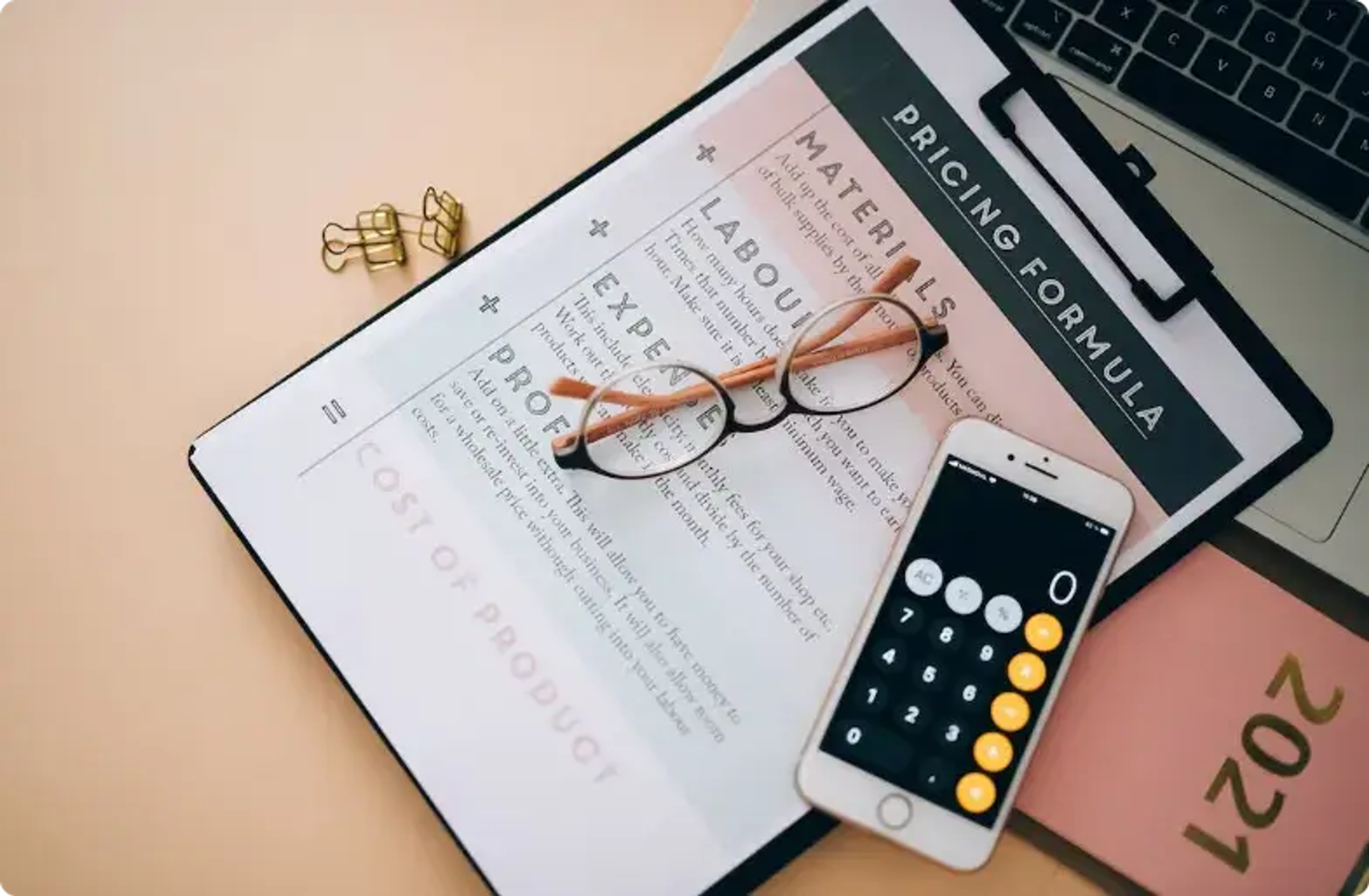 Workspace with pricing formula document, calculator, glasses, and laptop