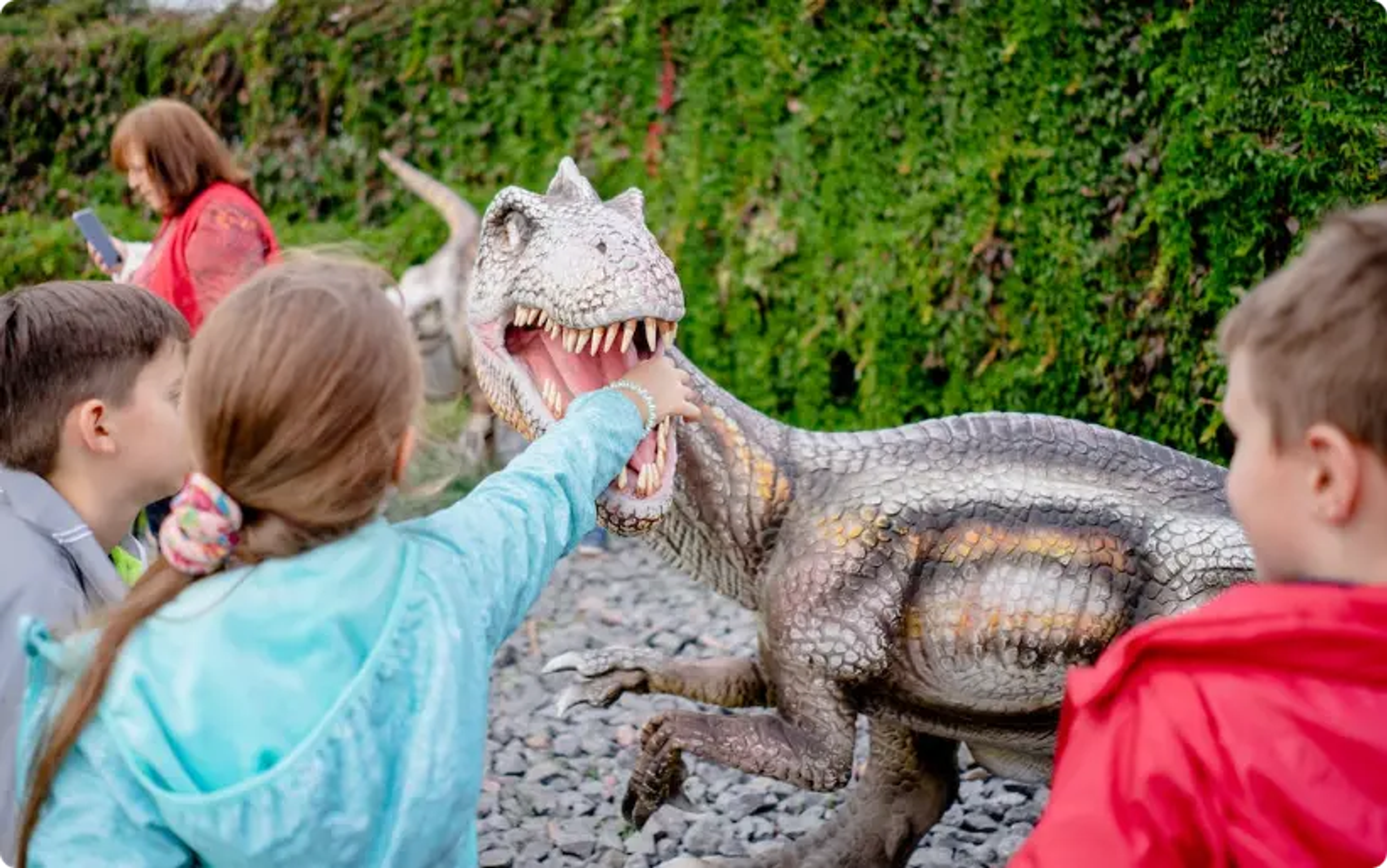 Children watch realistic dinosaur model with open mouth at outdoor exhibit