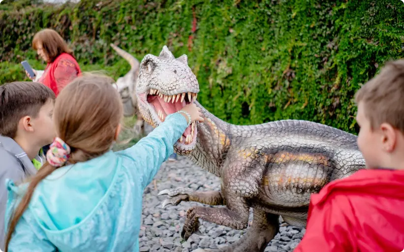 Kinderen kijken naar realistisch dinosaurusmodel met open mond bij buitenexpositie