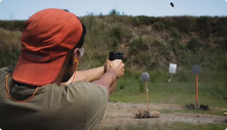 Pessoa com boné vermelho praticando tiro em um campo de tiro ao ar livre