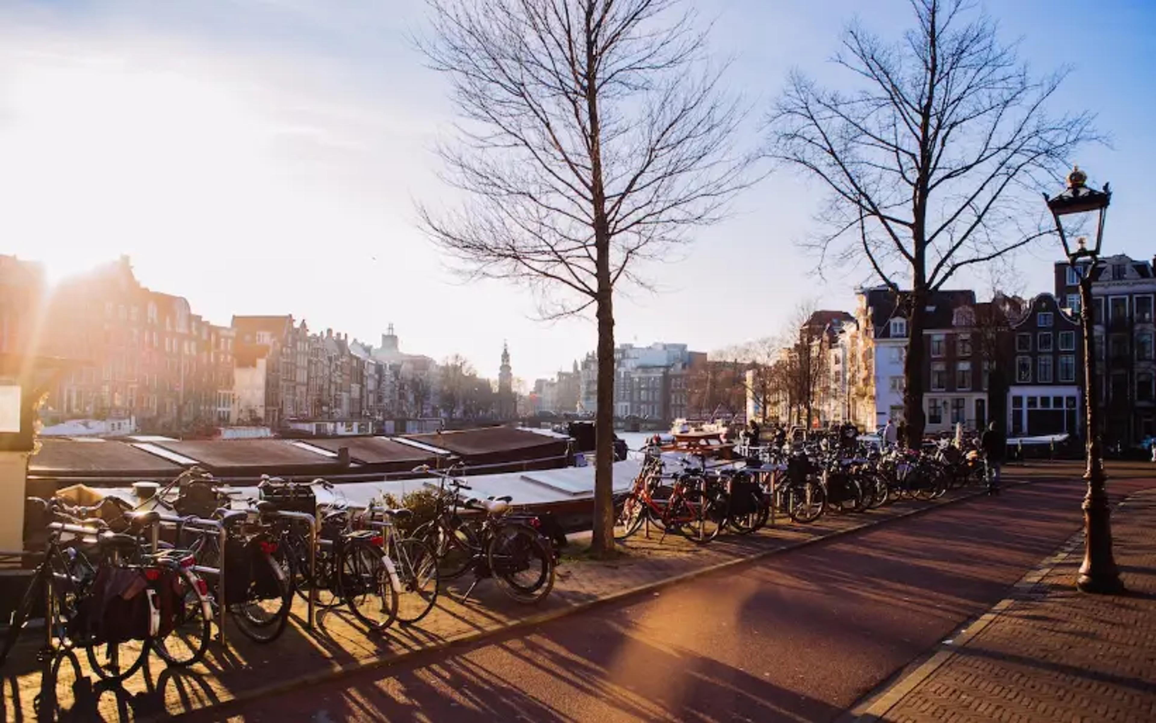 Canal de Amsterdã iluminado pelo sol com bicicletas estacionadas ao longo de edifícios históricos