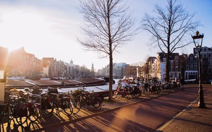 Canal de Amsterdã iluminado pelo sol com bicicletas estacionadas ao longo de edifícios históricos