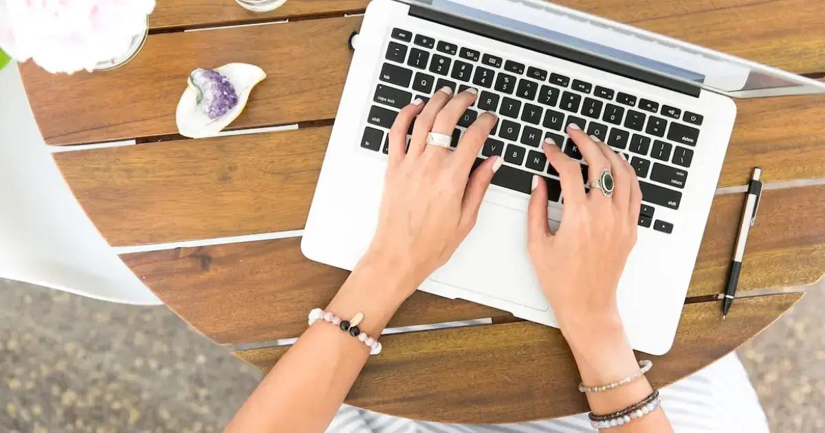Mains tapant sur un ordinateur portable à côté d'un stylo et d'un cristal