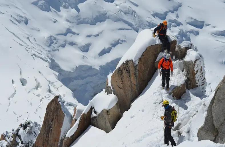 Mountain climbers navigate rocky, snow-covered peak with steep, challenging terrain