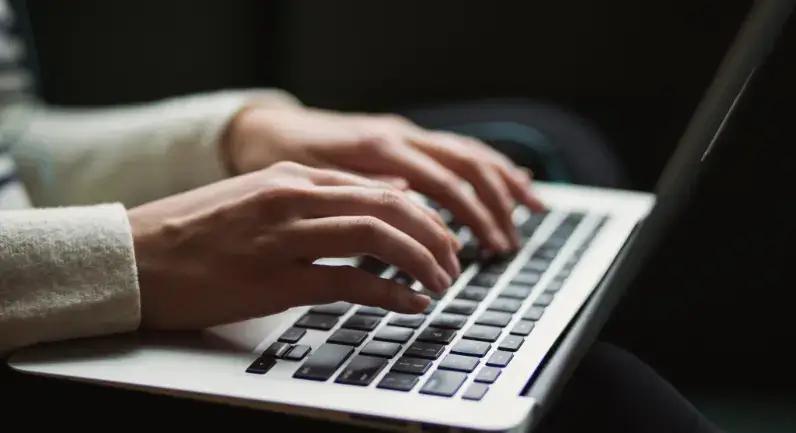 Handen die typen op een laptoptoetsenbord in een schemerige omgeving