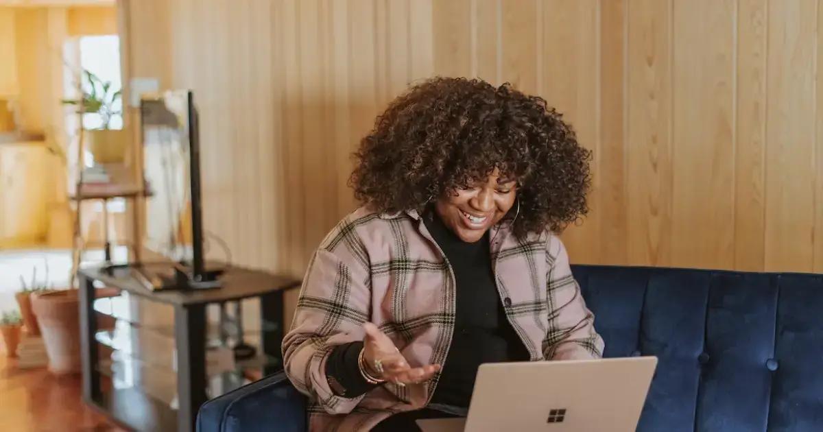 Vrouw glimlachend werkend op een laptop op een blauwe bank