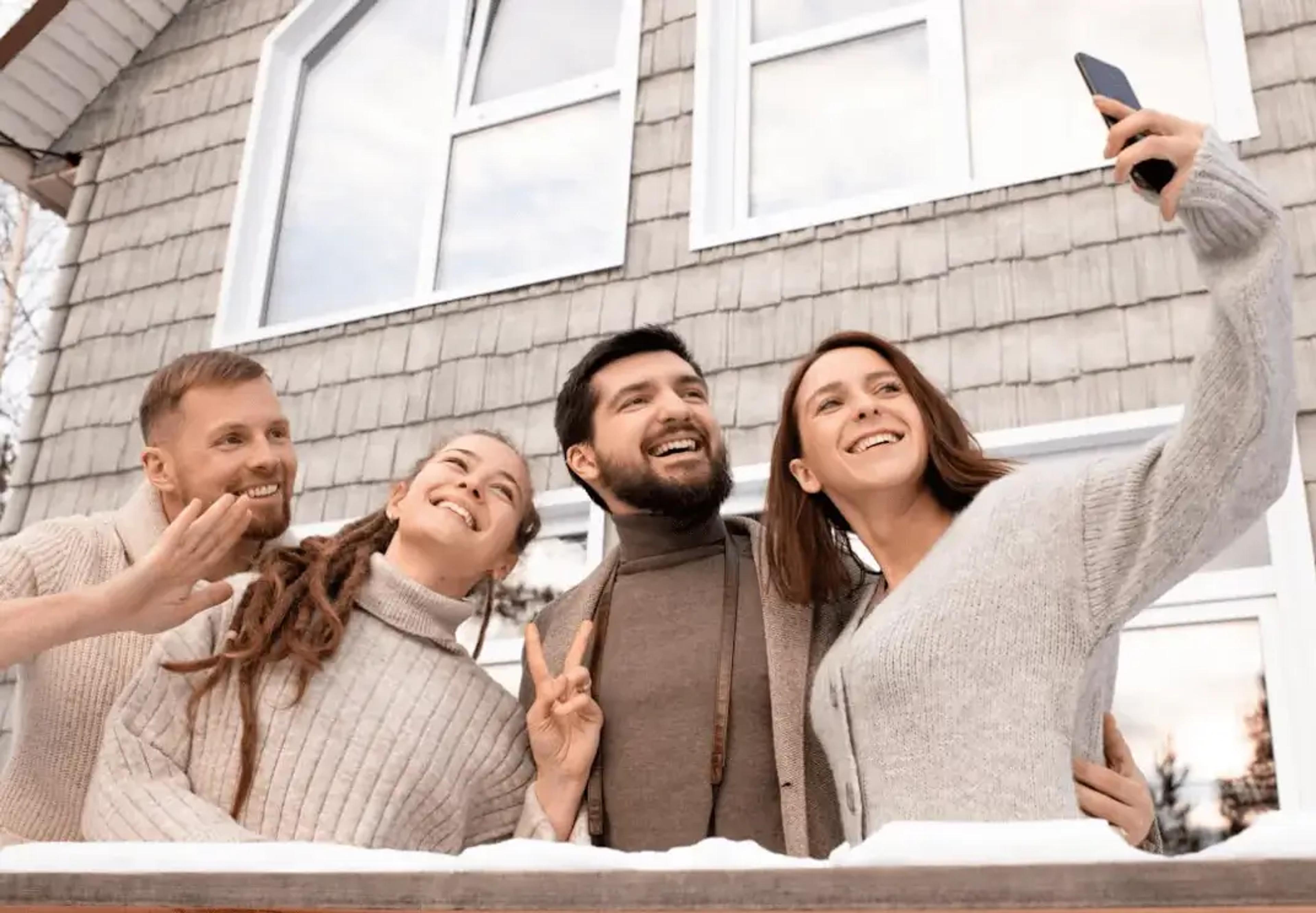 Fire grinende venner tager en selfie foran et hus om vinteren
