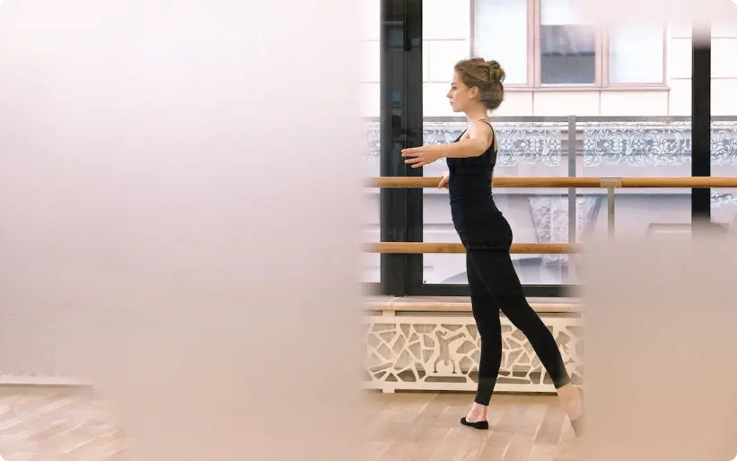 Ballerina che pratica balletto al barre in studio con pavimento in legno e finestre