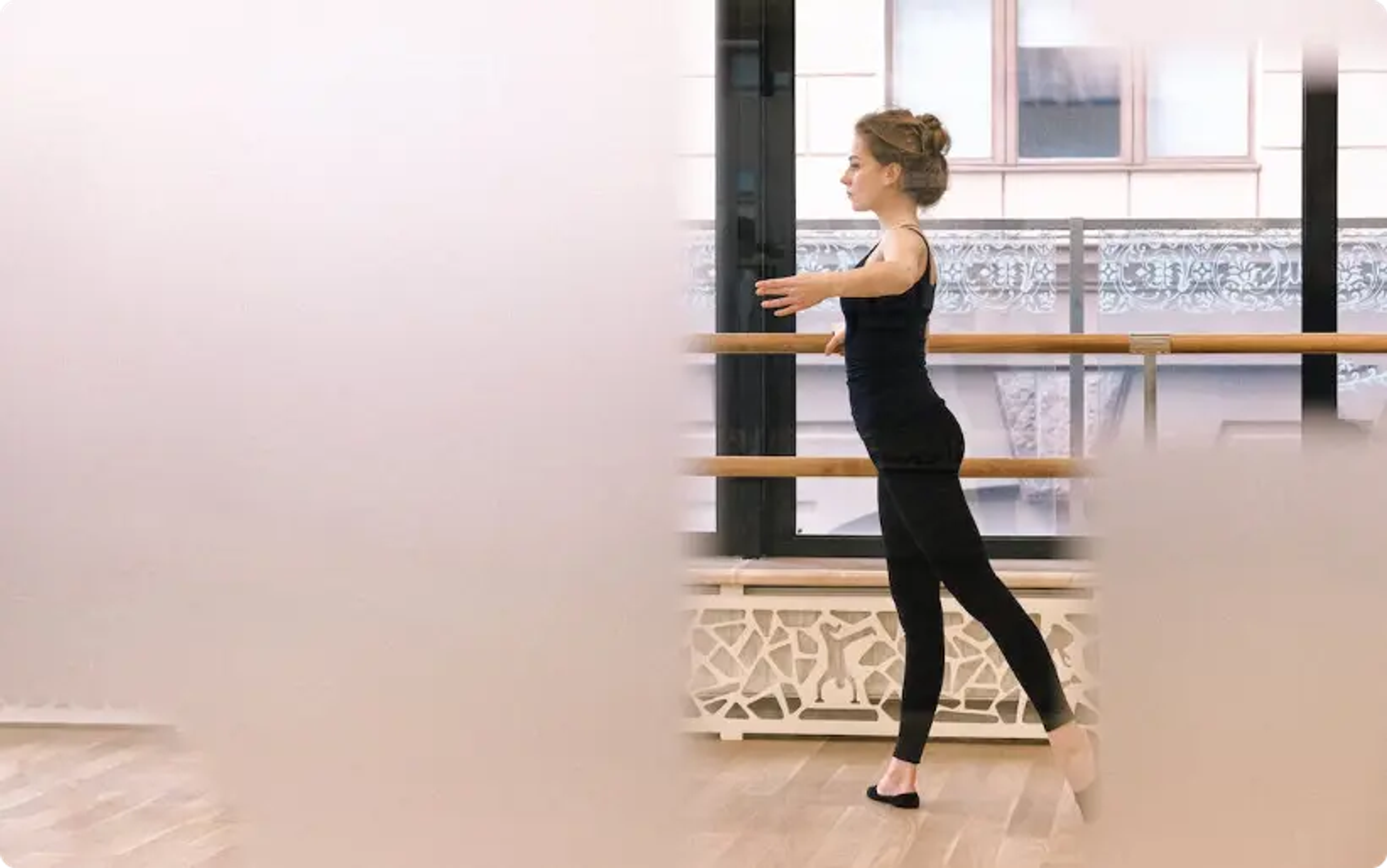 Tänzerin, die im Studio mit Holzfußboden und Fenstern Ballett an der Stange übt