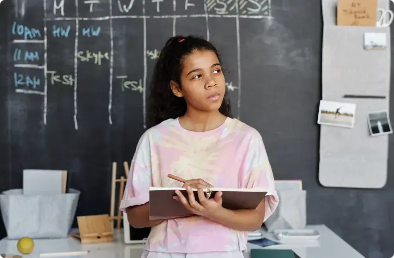Student in tie-dye shirt die bij een krijtbordschema staat met een notitieboekje