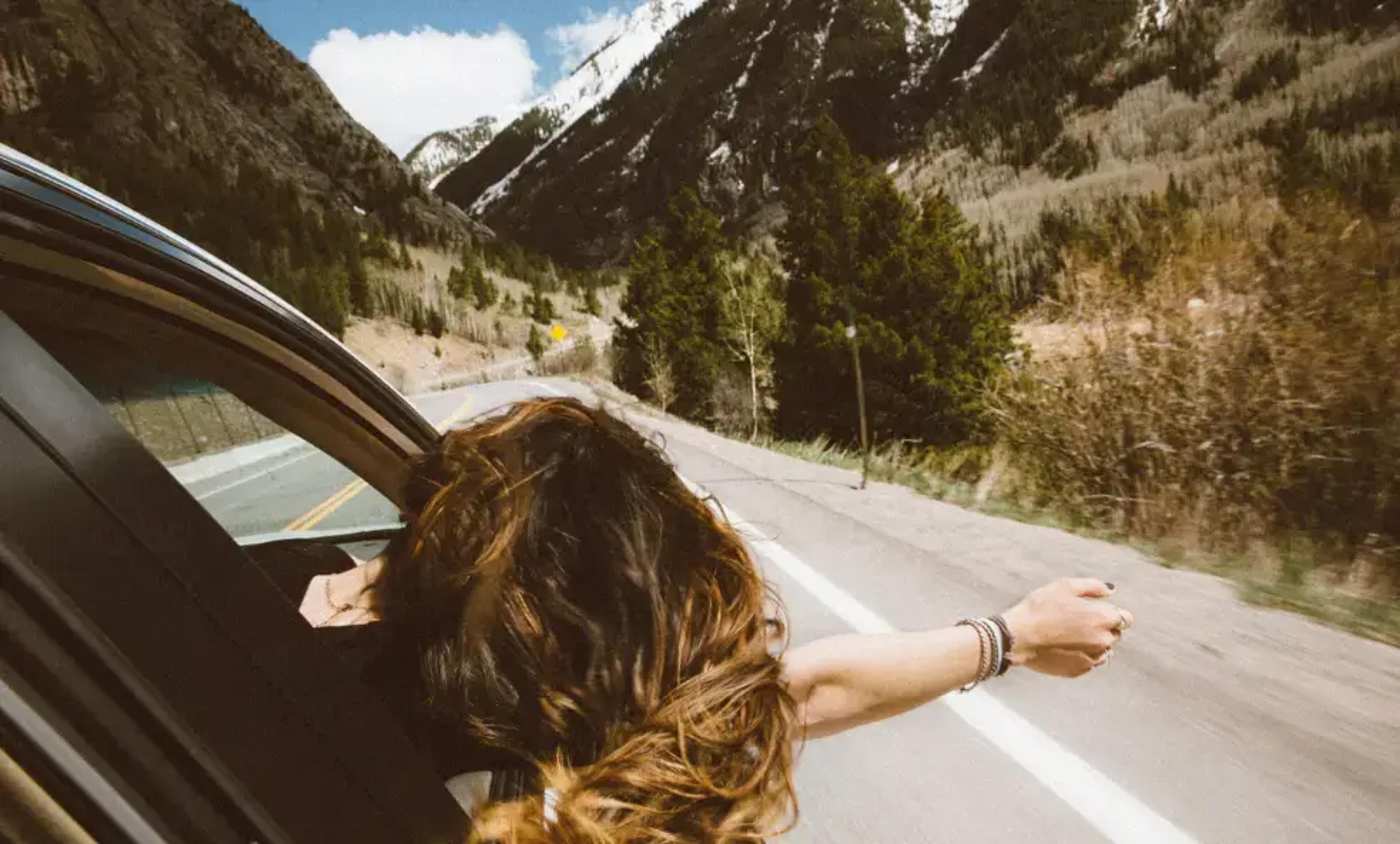 Személy élvezi a hegyi autóutat, karját az autó ablakán kinyújtva