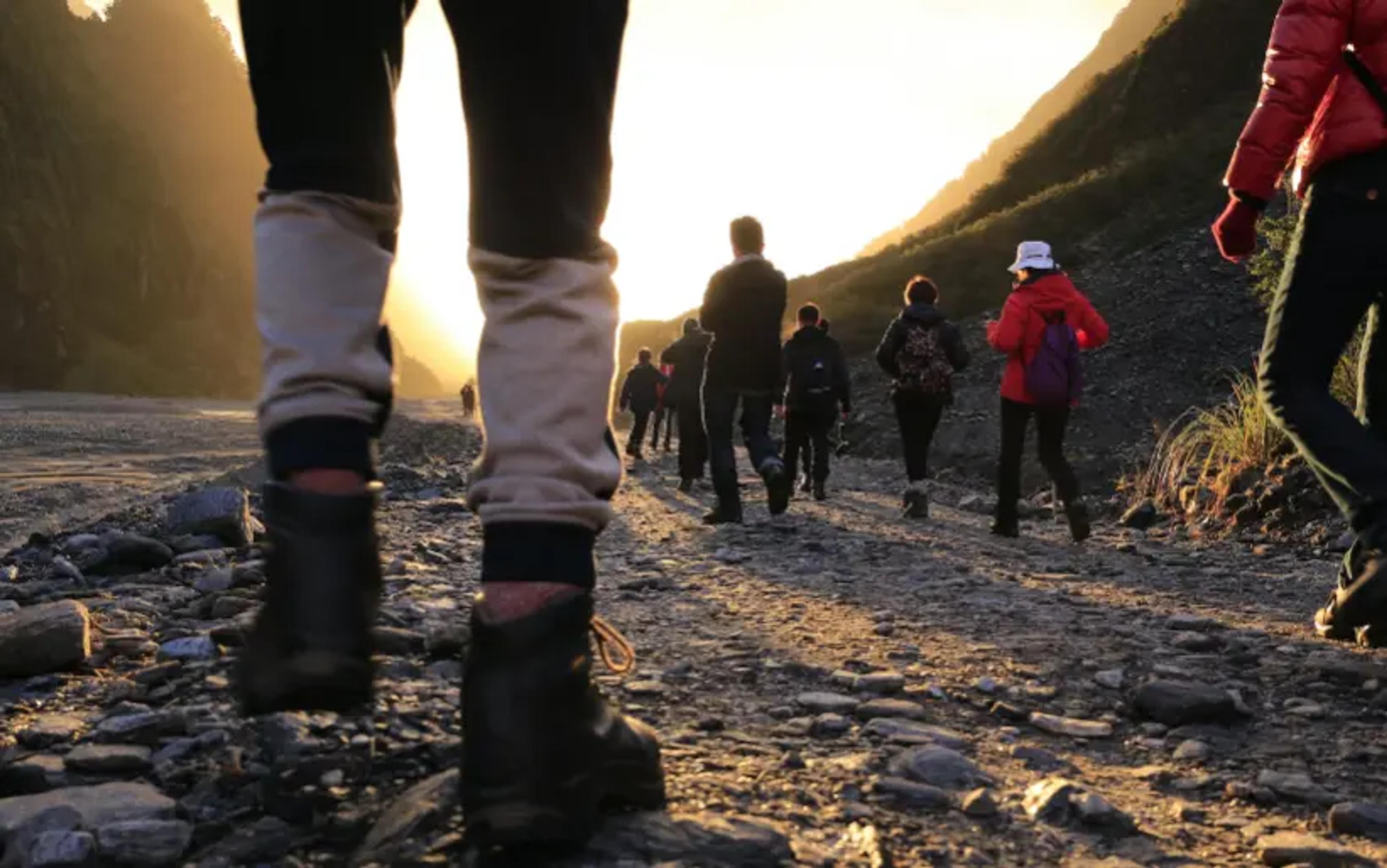 Randonneurs marchant sur un sentier rocheux au lever du soleil avec un arrière-plan de montagne