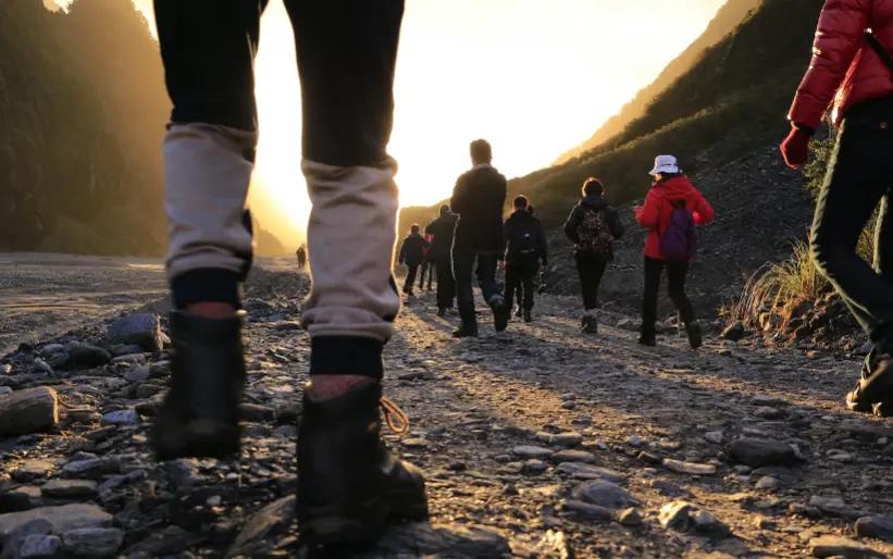 Randonneurs marchant sur un sentier rocheux au lever du soleil avec un arrière-plan de montagne