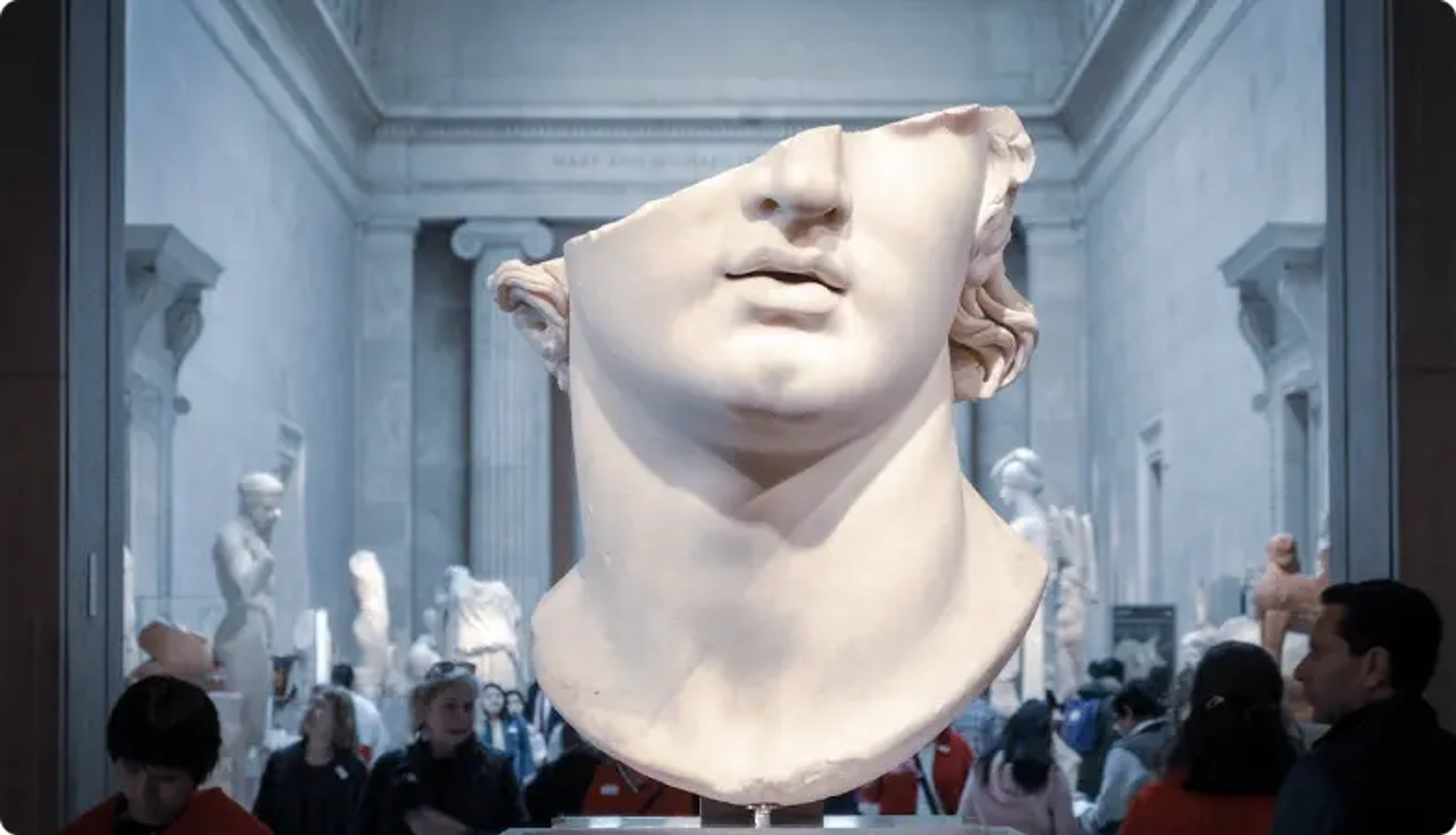 Large white marble sculpture head in museum gallery with visitors