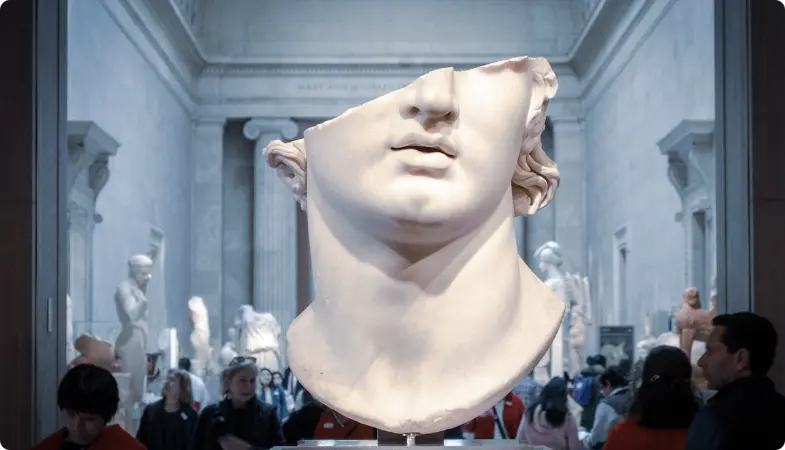 Large white marble sculpture head in museum gallery with visitors