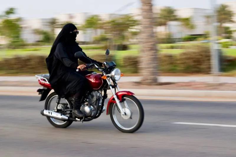 Woman in a black abaya riding a red motorcycle