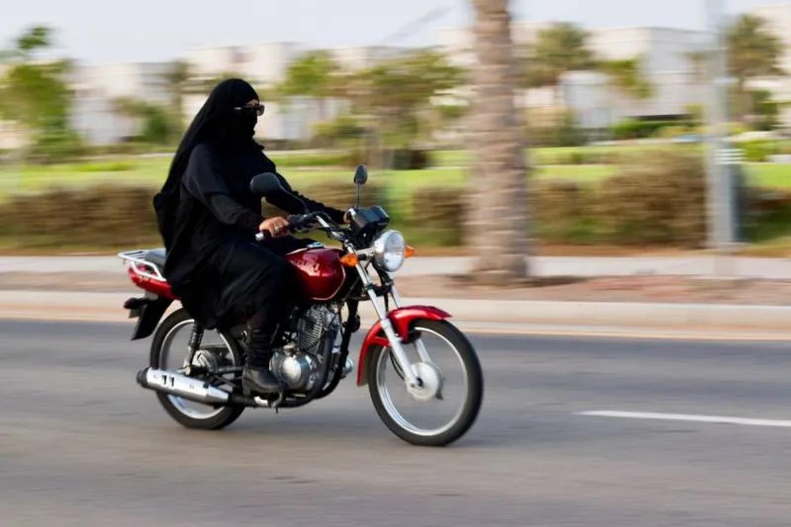 Woman in a black abaya riding a red motorcycle