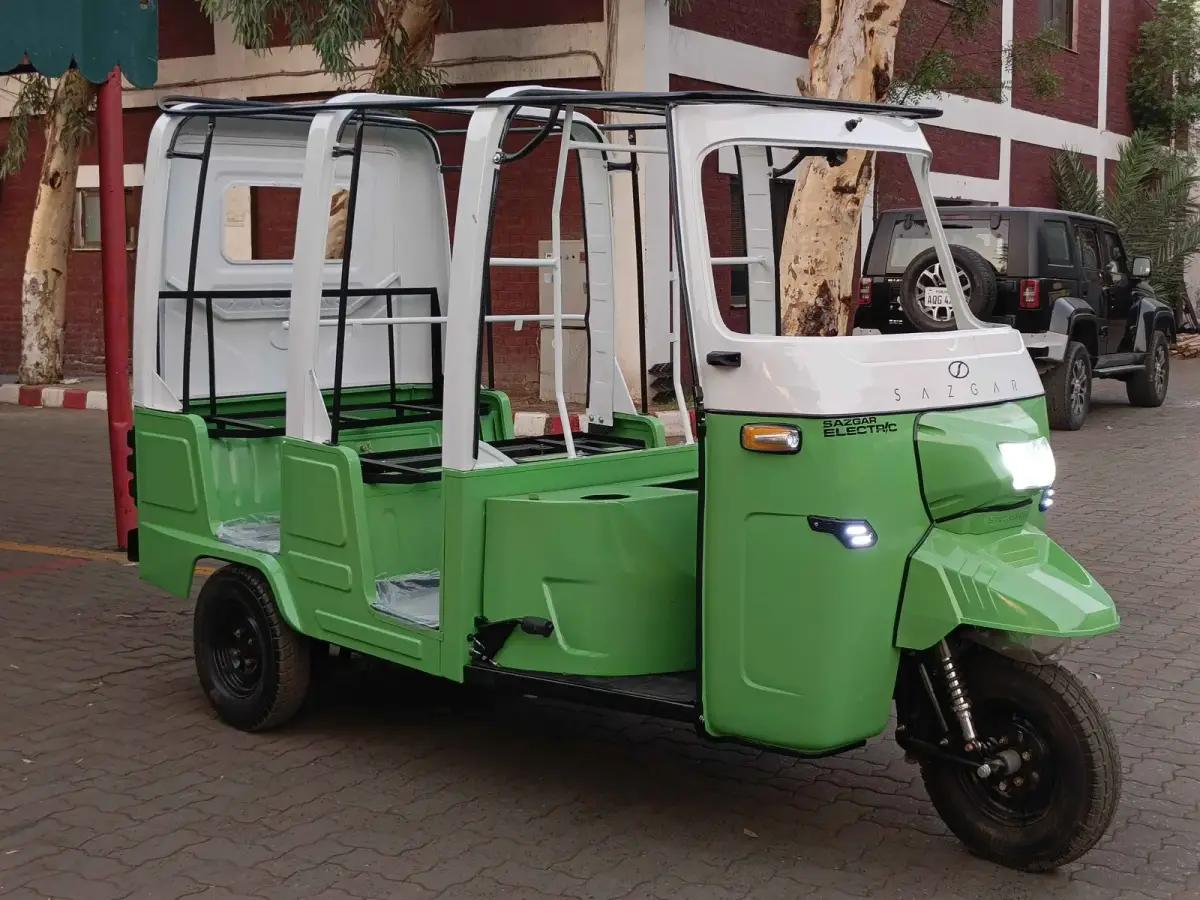 Open-frame green Sazgar electric rickshaw parked outside a brick building