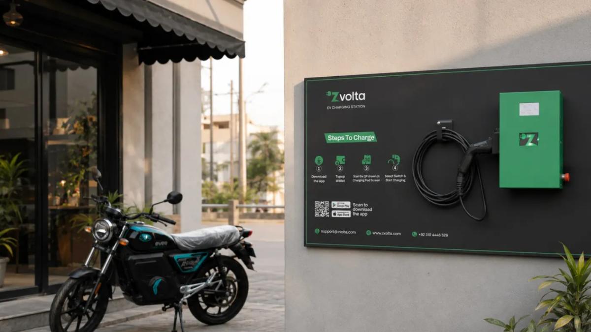 A Zvolta wall charger on a branded backplate outside a shop, with a motorbike charging