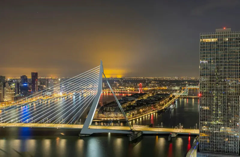 Hardlopers tijdens de DSW Bruggenloop Rotterdam over de verlichte Erasmusbrug bij schemering