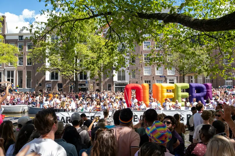 Drukke Amsterdamse gracht tijdens Koningsdag met mensen in het oranje en bootjes vol feestvierders