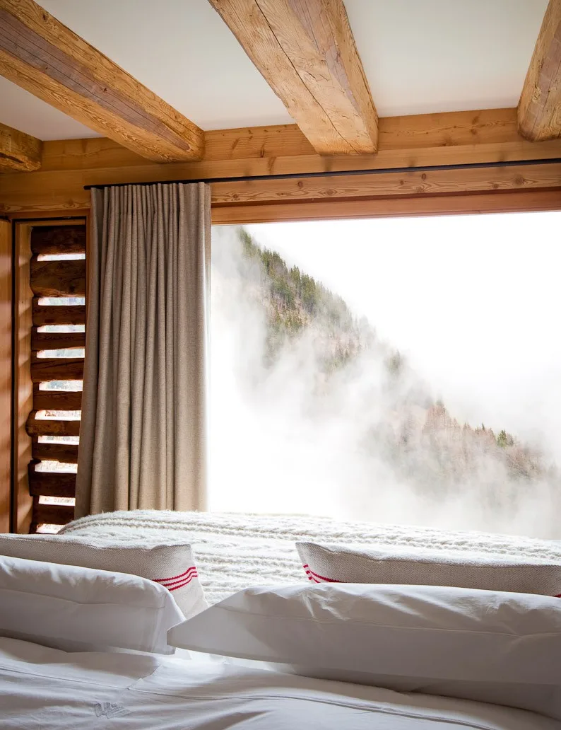 Bedroom with wood beams and a misty forested mountain view at Montagne Alternative hotel, Switzerland