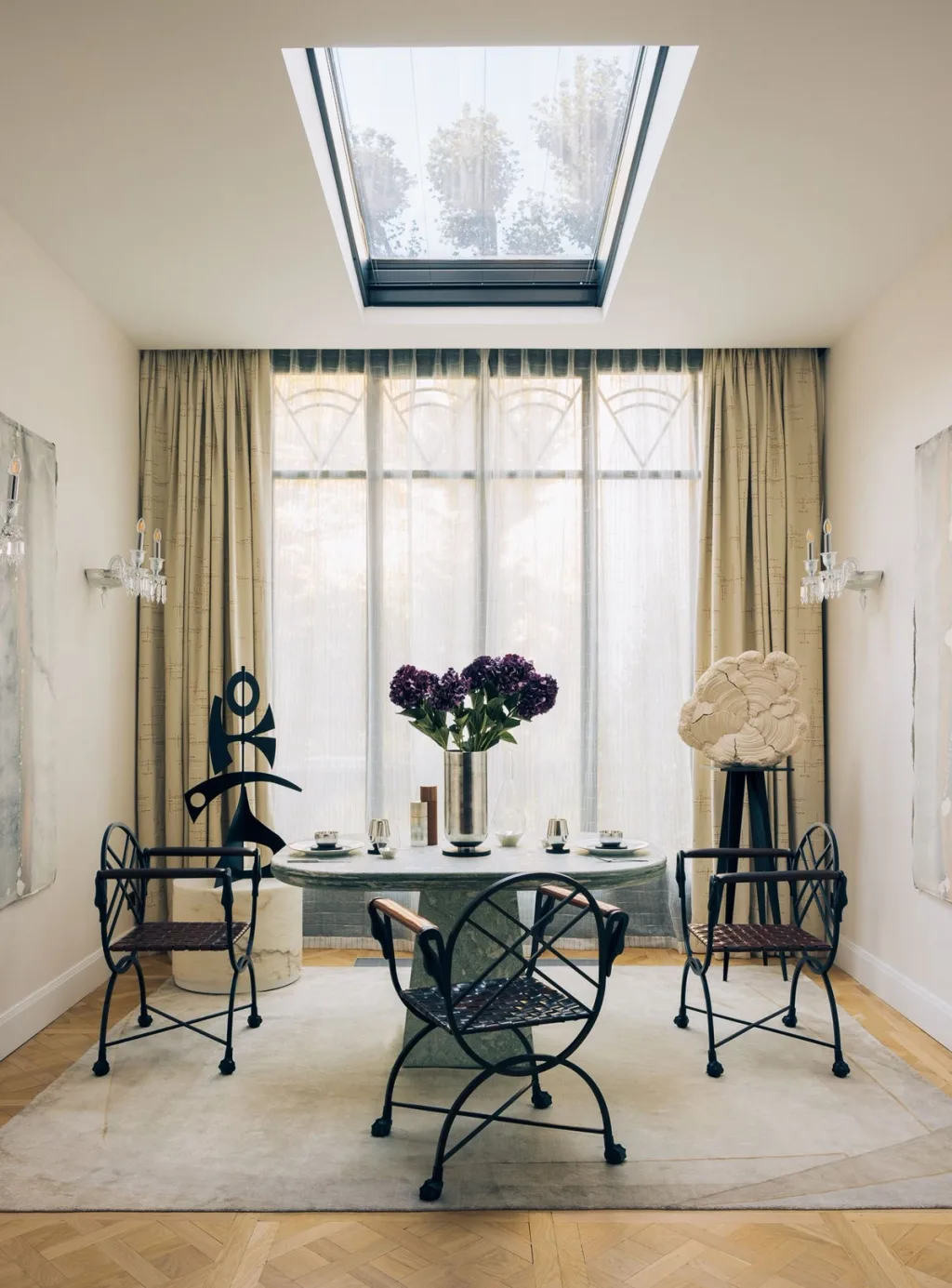 Round dining table and sculptural black chairs beneath a skylight in a Stéphanie Coutas interior, Paris