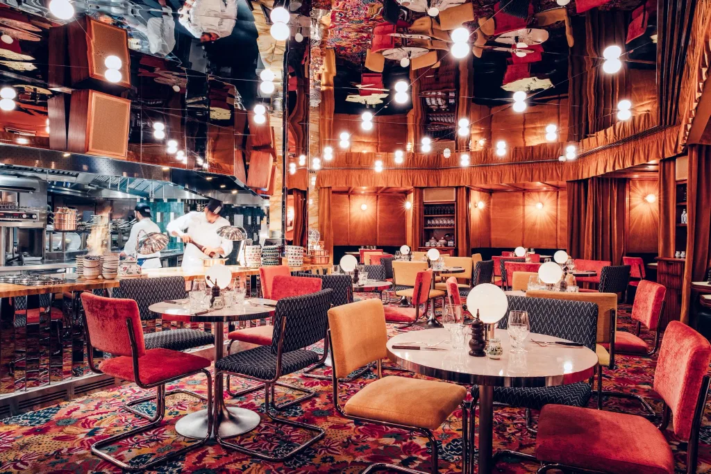Red and orange dining chairs beneath a mirrored ceiling beside the kitchen at Big Mamma, UK