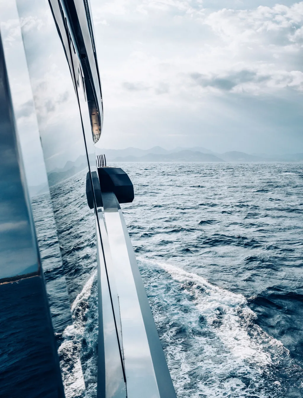 Waves and distant hills reflected along the polished side of the Atlante yacht