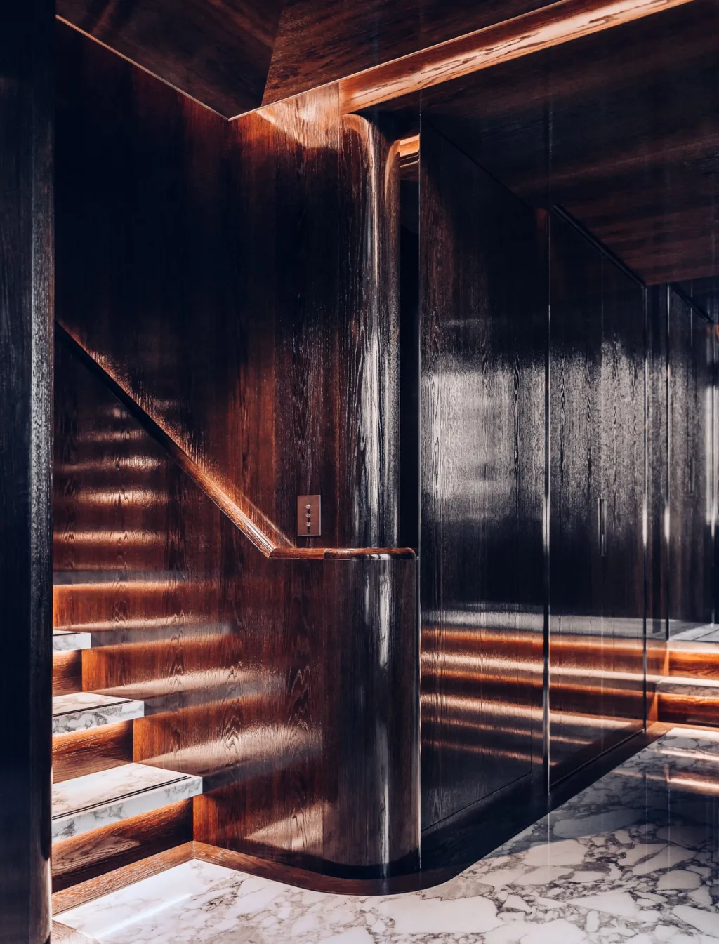 Illuminated staircase curving beside glossy dark wood walls aboard the Atlante yacht