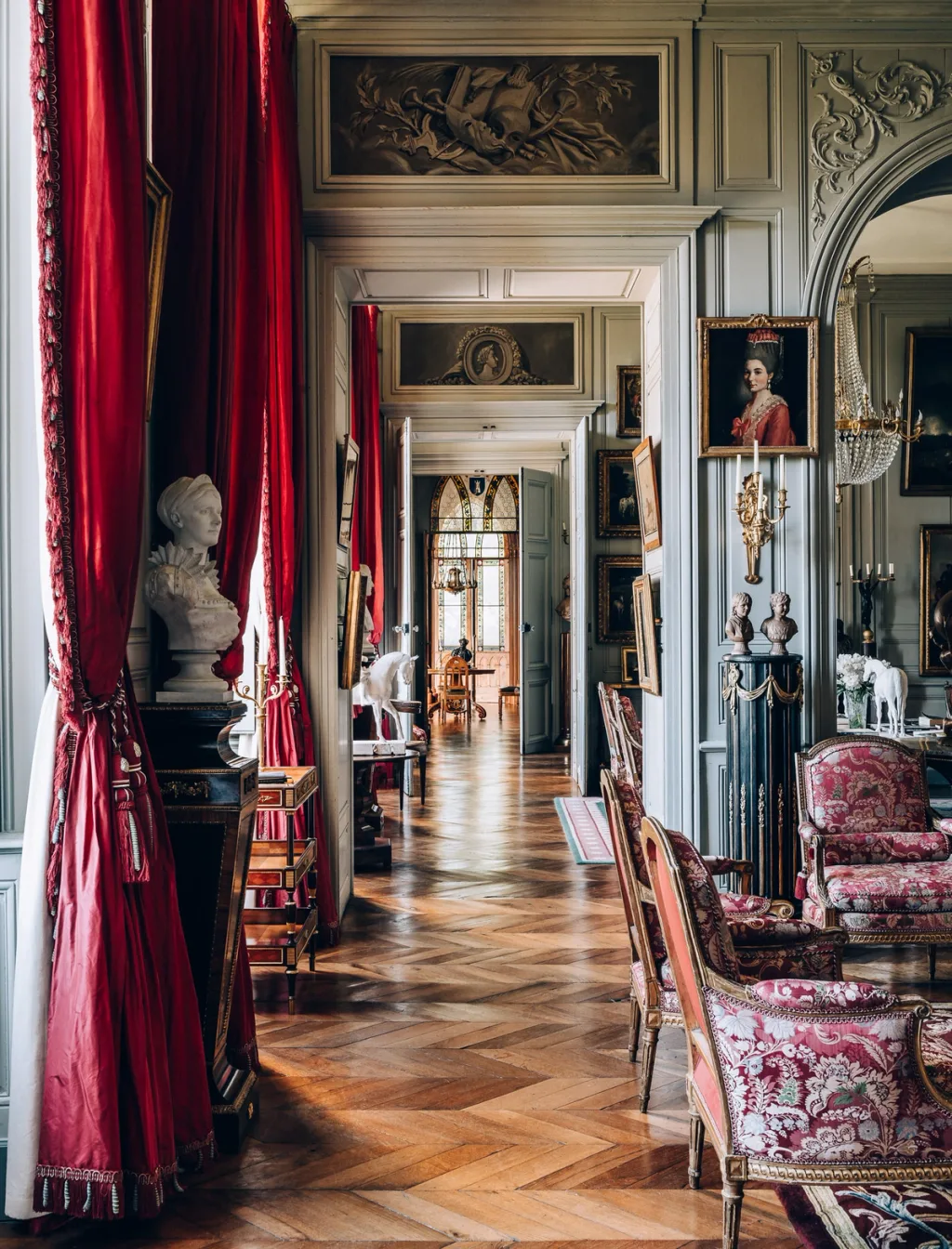 Interconnecting salons with red curtains, portraits and patterned chairs at Chateau de Digoine