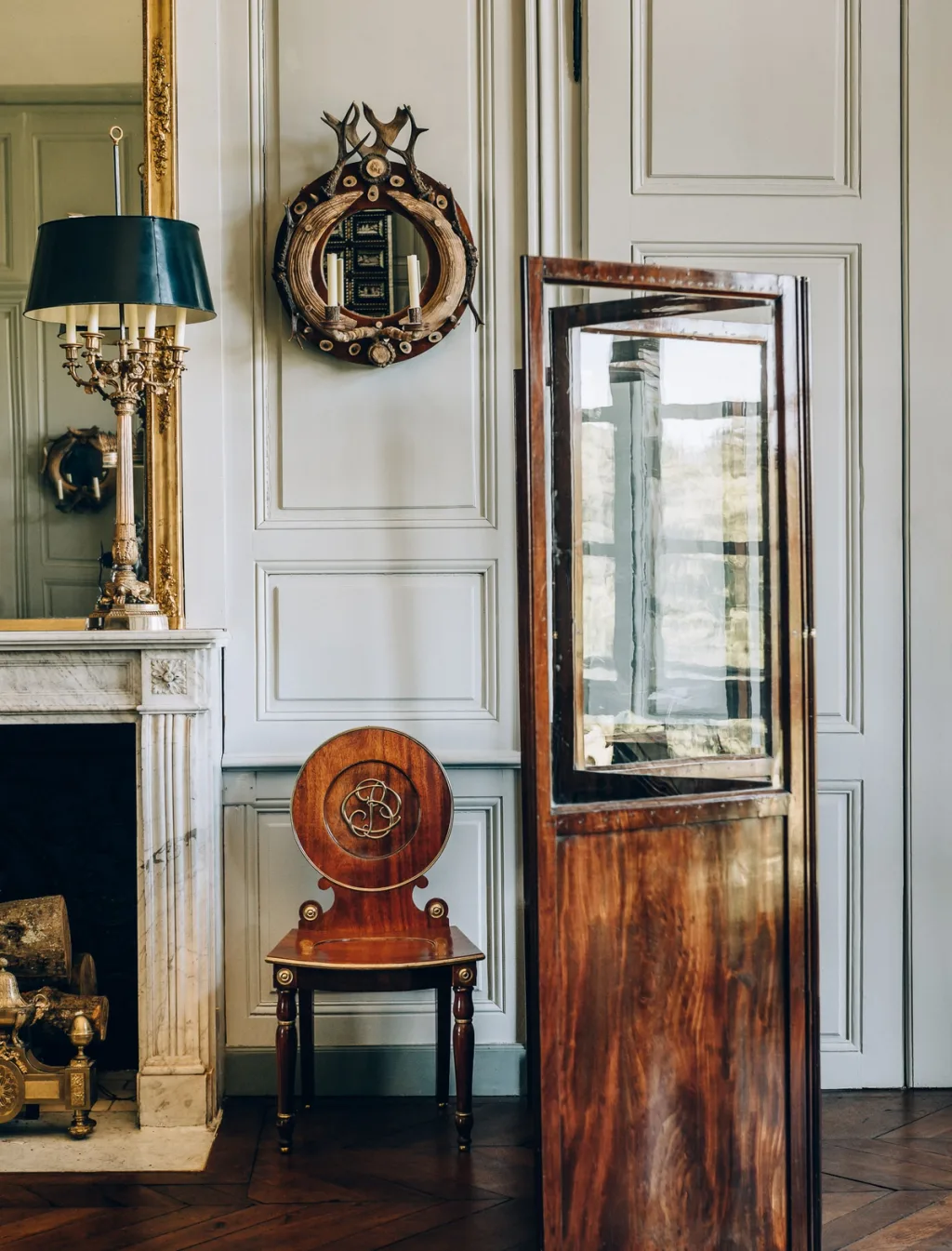 Wooden display case and round-backed chair beside a fireplace at Chateau de Digoine