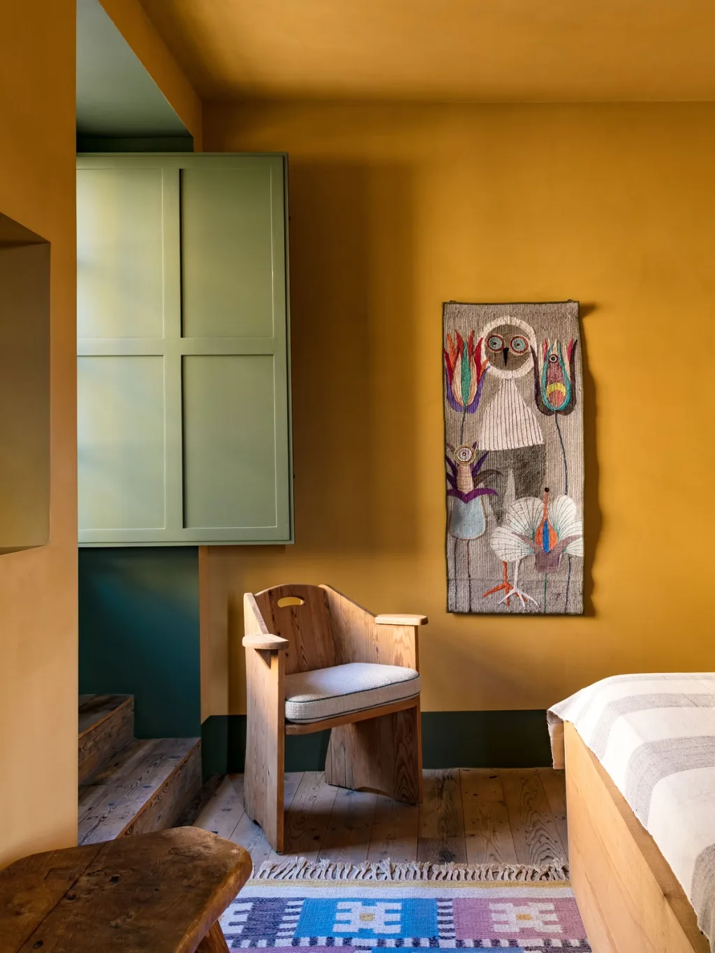 Wooden armchair and owl wall hanging in a yellow bedroom at Fabrègues, Pierre Yovanovitch
