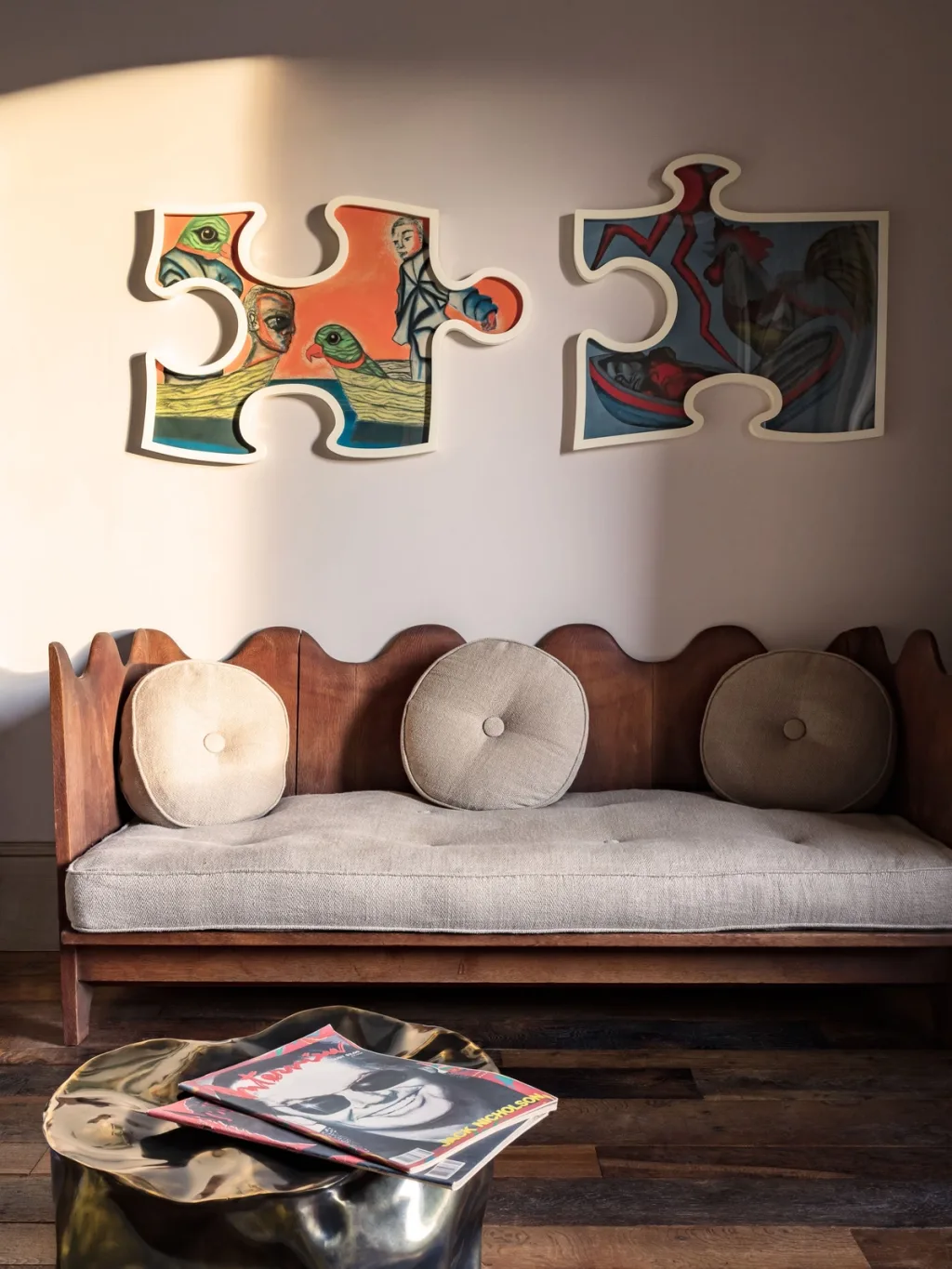 Scalloped wooden sofa beneath two puzzle-shaped artworks at Fabrègues, Pierre Yovanovitch