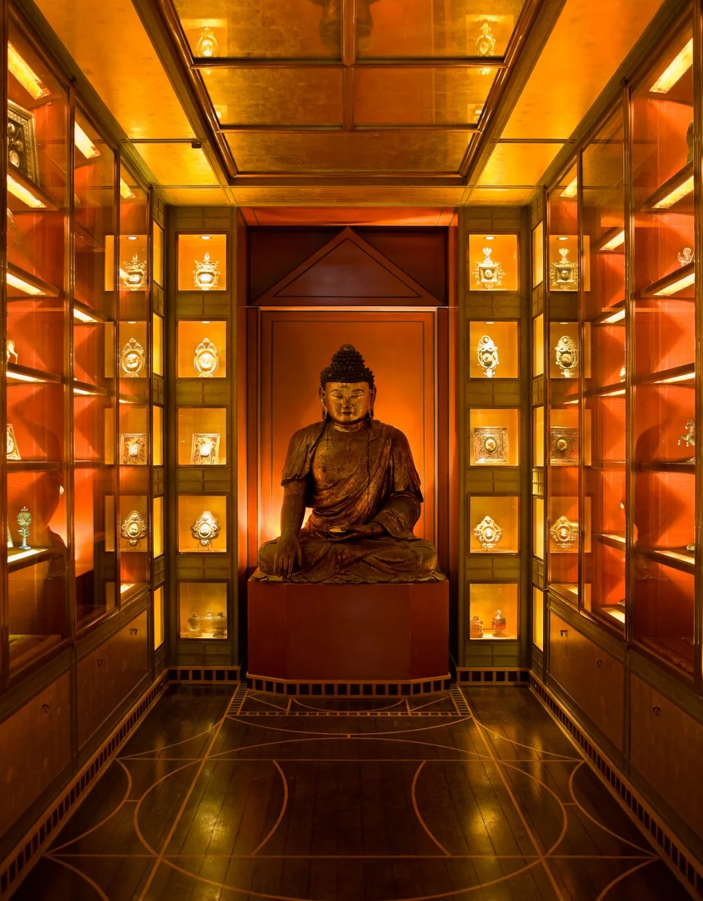 Seated Buddha sculpture among warmly lit display cabinets, Yves Saint Laurent, Paris