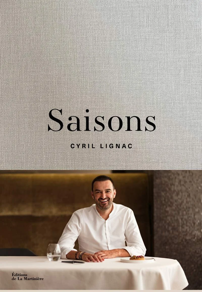Cover of Cyril Lignac’s Saisons cookbook, with the chef seated at a white-clothed table