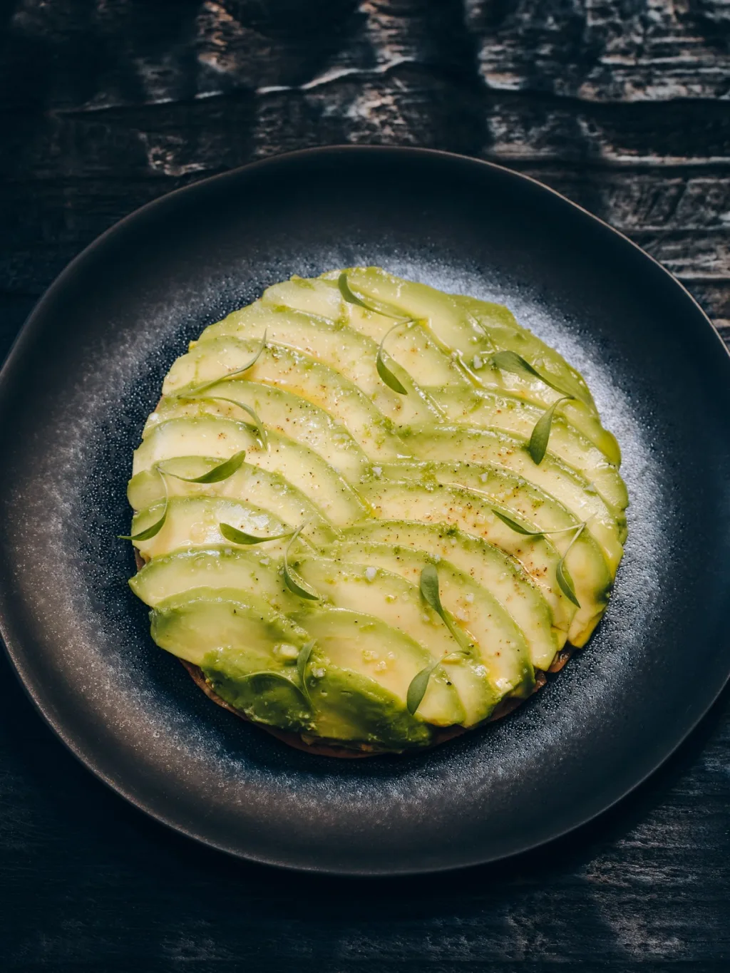 Overlapping green slices with tiny leaves on a dark plate for Cyril Lignac’s Saisons cookbook