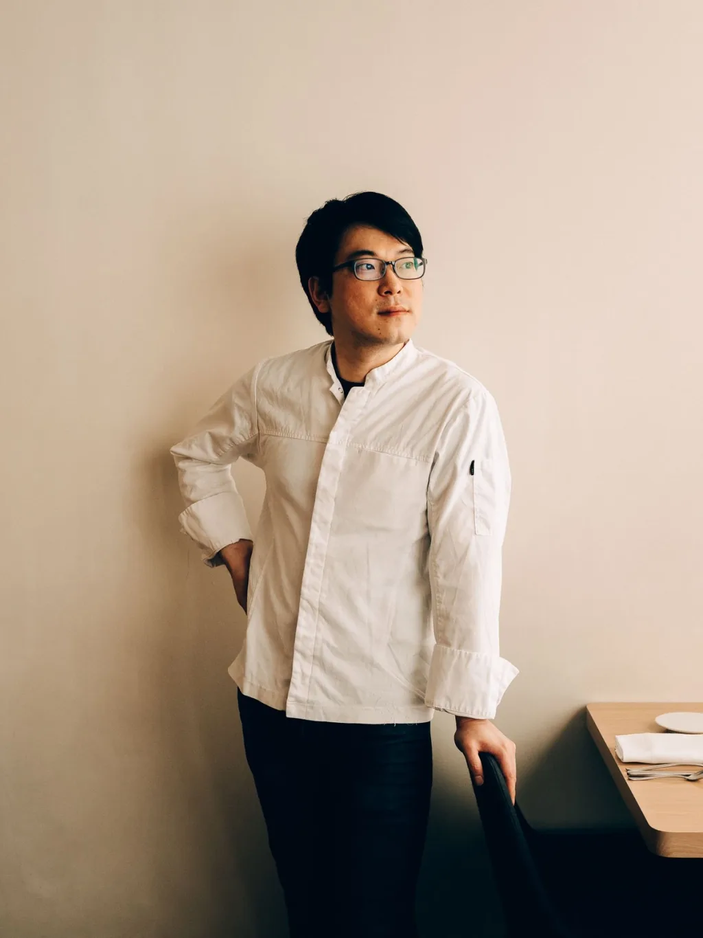 Chef wearing glasses and a white jacket beside a restaurant dining table in Lyon